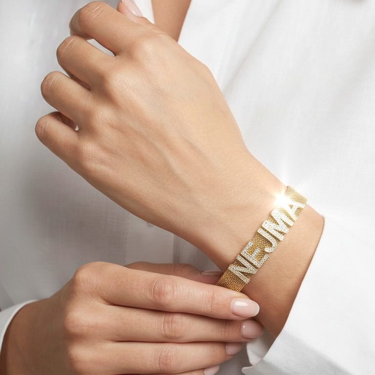 Bracelet personnalisé en maille prénom strass Femme portant un bracelet en maille dorée personnalisé avec le prénom Nejma en lettres strass. Création sur-mesure Rêve Étoilé.