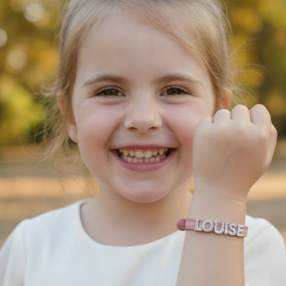 Avis Client Bijou Enfant - Rêve Étoilé Avis client Rêve Étoilé avec une petite fille souriante portant un bracelet personnalisé en cuir rose au prénom de Louise